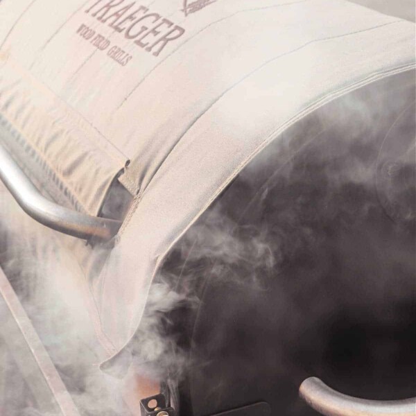 Close-up of a Traeger grill with smoke rising, partially obscuring the logo on this best smoker for beginners.