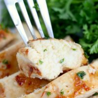 A fork holds a piece of juicy chicken breast, perfectly cooked in the Ninja Foodi, garnished with chopped herbs. The chicken is sliced with visible grill marks. Fresh green parsley or cilantro adorns the background, enhancing its visual appeal.