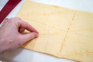 A hand pinching perforations on crescent rolls dough