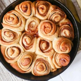 A skillet brimming with freshly baked, golden-brown cinnamon rolls—crafted with a no-yeast recipe—rests on a rustic wooden surface.