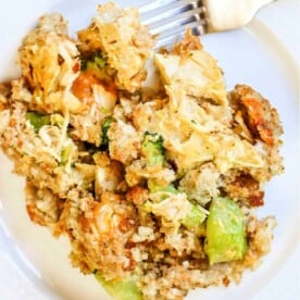 A plate of vegetable stuffing with broccoli, carrots, and bread crumbs sits next to a fork, offering a delightful taste that echoes the flavors of a cheesy chicken broccoli casserole without the meat.