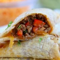 A close-up of two air fryer empanadas, one cut open to reveal a filling of ground meat and chopped red peppers, garnished with herbs.