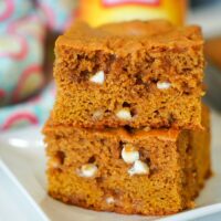 A pair of pumpkin blondies, brimming with white chocolate chips, is temptingly stacked on a plate.