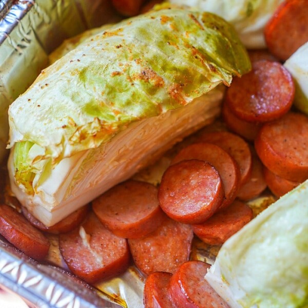 In a foil tray, smoked sausage slices pair perfectly with cabbage wedges, ready for cooking.