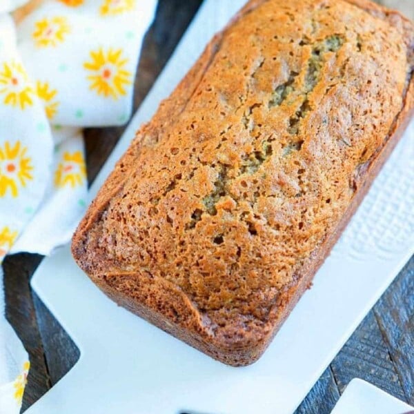 A loaf of moist zucchini bread sits on a white cutting board, accompanied by a yellow floral napkin, reminiscent of a delightful zucchini bread recipe.