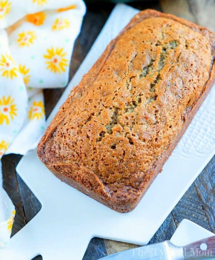 A loaf of moist zucchini bread sits on a white cutting board, accompanied by a yellow floral napkin, reminiscent of a delightful zucchini bread recipe.