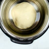 A ball of dough rests in a metal pot on a light background, showcasing the ideal setup for those learning how to proof dough in an Instant Pot.