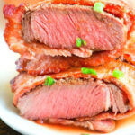 Close-up of a sliced, medium-rare air fryer steak garnished with chopped green onions on a white plate.