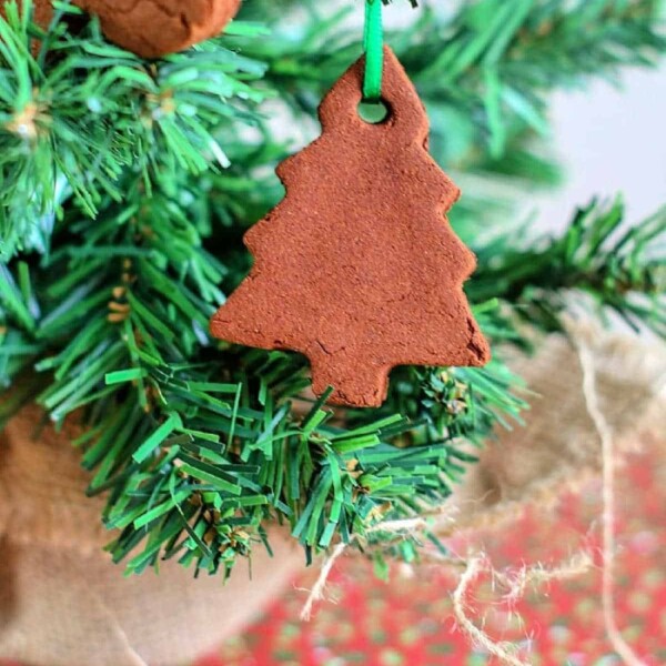 A delightful cinnamon ornament, crafted from a cherished recipe, hangs gracefully on an evergreen branch in the shape of a Christmas tree.