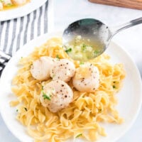 Plate of pasta topped with perfectly seared air fryer scallops and savory sauce, served with a spoon and striped napkin.