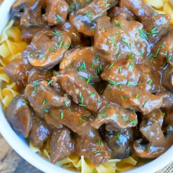 Instant Pot beef tips stroganoff with mushrooms, served over egg noodles and garnished with chopped herbs in a white bowl.