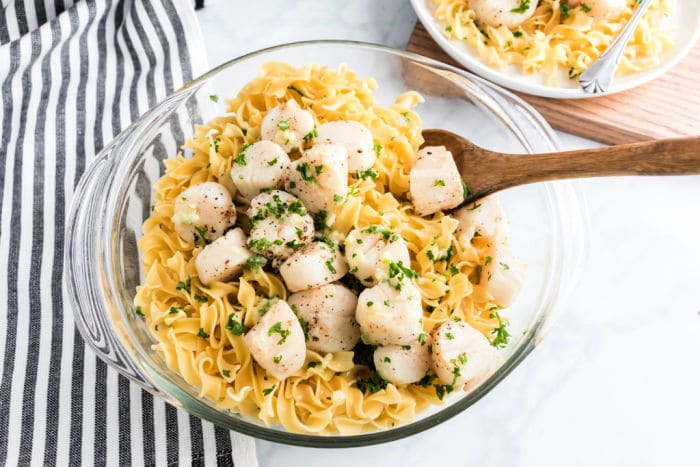 Bowl of pasta topped with air fryer scallops and chopped herbs, served with a wooden spoon.