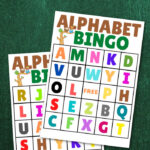 Two vibrant alphabet bingo cards rest on a green textured background, ready for your next game.