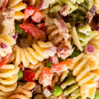 Close-up of a colorful bacon pasta salad featuring rotini, crispy bacon, red peppers, peas, and diced onions.