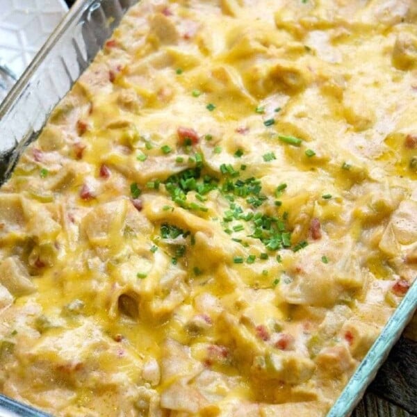 Baked chicken tortilla casserole with melted cheese and chopped herbs on top in a glass dish.