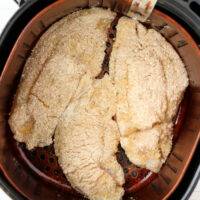 Air fryer catfish fillets in a basket on a light-colored surface.