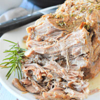 Shredded pork with herbs on a white plate, garnished with a sprig of rosemary. A frozen pork shoulder is transformed in the Instant Pot, with apples adding to the scene in the background.