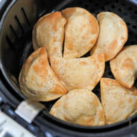 Golden brown frozen pierogies in an air fryer basket, lightly seasoned with pepper.