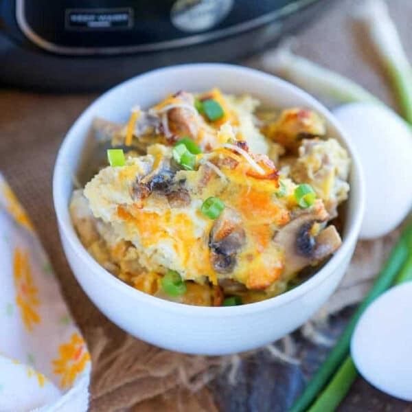 Bowl of cheesy breakfast casserole with green onions, made in the Ninja Foodi, next to eggs and a kitchen appliance in the background.