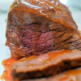 A close-up of a perfectly cooked tri tip in pressure cooker topped with rich gravy.