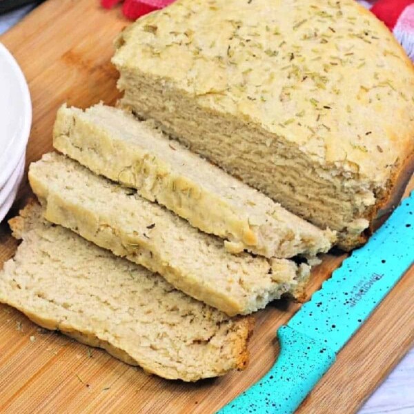 A loaf of slow cooker bread, partially sliced, rests on a wooden cutting board beside a blue-handled knife.