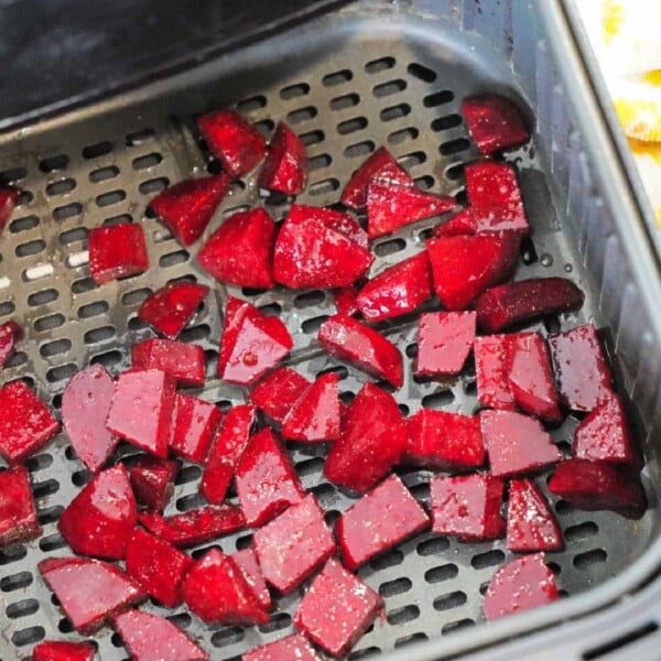 Diced red beets placed in an air fryer basket, ready for cooking. These air fryer beets are spread out evenly across the perforated surface.