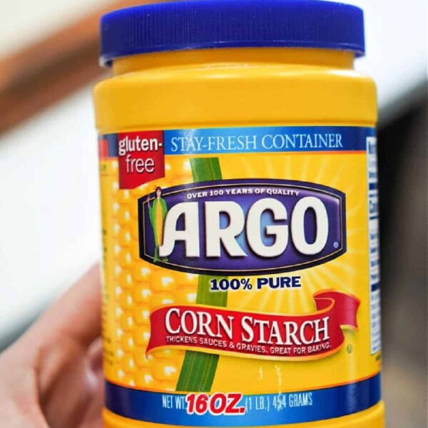 A hand holds a container of Argo 100% pure corn starch, perfect for those seeking a gluten-free option to thicken their favorite dishes. Weighing in at 16 oz (454 grams), it's the ideal choice for any culinary endeavor.