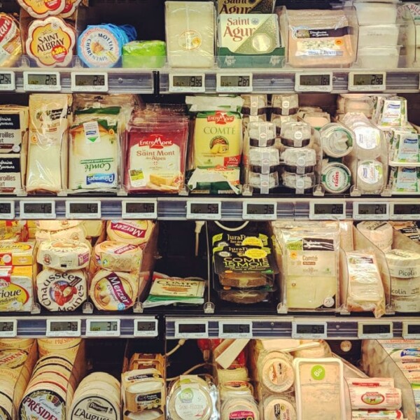 A supermarket display brimming with different kinds of cheese showcases various types of packaged delights. The shelves are stocked with diverse brands and shapes, including round and rectangular packages. These cheeses are meticulously organized in multiple rows, each adorned with visible price tags.