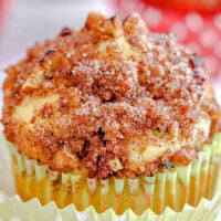 Close-up of an apple zucchini muffin topped with crumbly cinnamon sugar and nuts, nestled in a yellow paper liner.