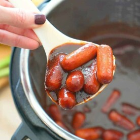 A person holds a ladle filled with small sausages in a rich, brown sauce above an Instant Pot, perfecting the ultimate cocktail wiener recipe.