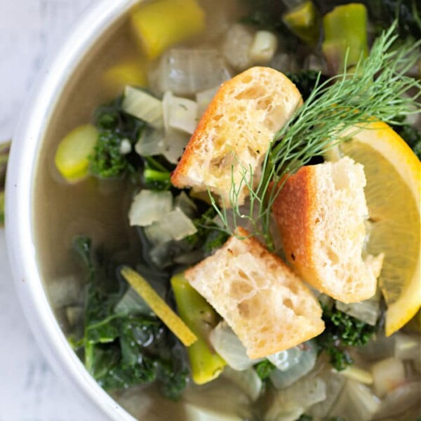 Bowl of asparagus and spinach soup topped with croutons, garnished with a lemon slice and dill.