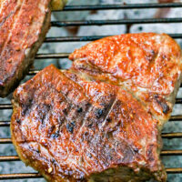 Two pieces of grilled steak on a metal grate, showcasing perfect grill marks and a browned finish—a testament to the best grilled steak recipe.