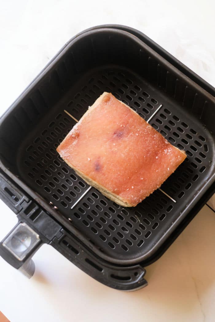 A slice of pork belly being toasted inside an air fryer basket pairs perfectly with the savory flavors of instant pot pork belly.