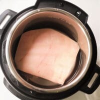 A square piece of pork belly in an Instant Pot, submerged in water.