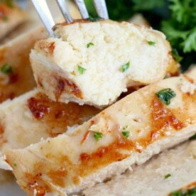 Close-up of chicken slices on a fork, expertly reheated in an air fryer for perfect crispness, garnished with herbs. A side of greens adds a vibrant touch in the background.