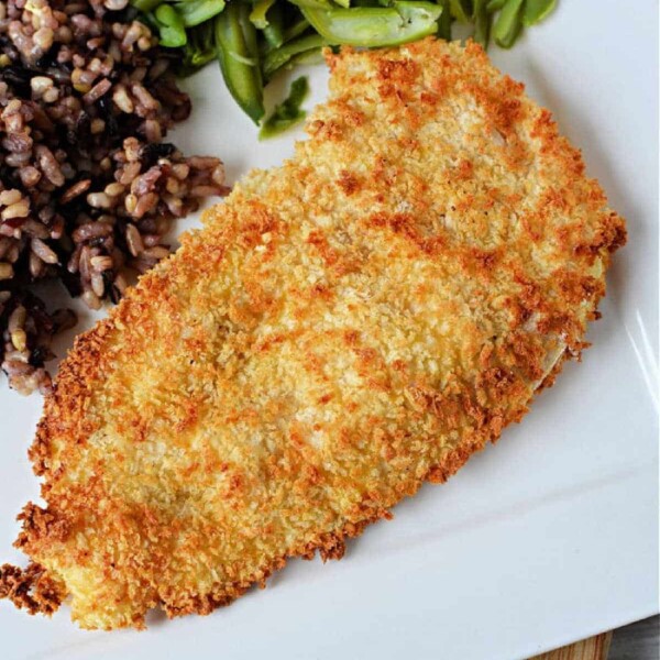 A breaded chicken cutlets sits elegantly on a plate alongside vibrant green beans and a medley of mixed rice, creating an inviting meal reminiscent of crispy chicken cutlets made effortlessly in an air fryer.