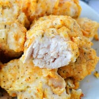 A plate of golden brown, air fryer-fried chicken breast pieces, one with a bite taken out, reveals the tender white meat inside.