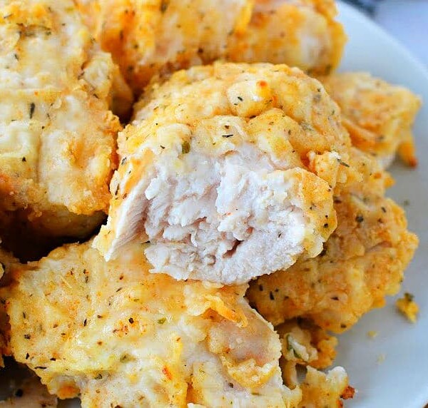 A plate of golden brown, air fryer-fried chicken breast pieces, one with a bite taken out, reveals the tender white meat inside.