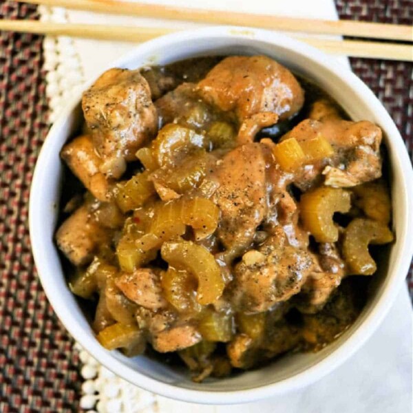 Bowl of Instant Pot black pepper chicken and celery stir-fry with sauce, placed on a white napkin, accompanied by chopsticks.