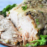 Frozen pork roast cooked in an Instant Pot with herbs, sliced and served on a plate garnished with fresh parsley.