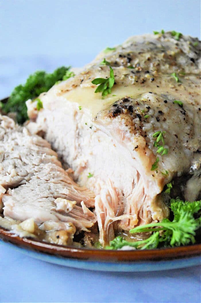 Frozen pork roast cooked in an Instant Pot with herbs, sliced and served on a plate garnished with fresh parsley.