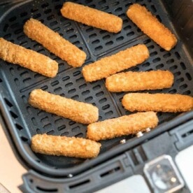 Frozen mozzarella sticks are neatly arranged in an air fryer basket, ready to be cooked.