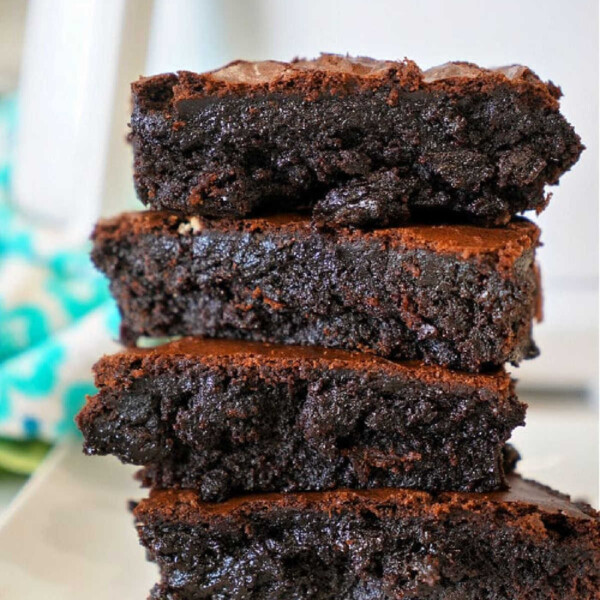 Stack of four thick, fudgy brownies on a white plate with a blurred background, showcasing how to make brownies out of cake mix for an easy twist on a classic treat.