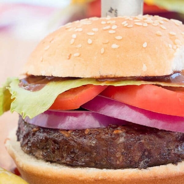 A juicy smoked burger with lettuce, tomato, and onion, topped with sauce and skewered with a knife on a wooden board.