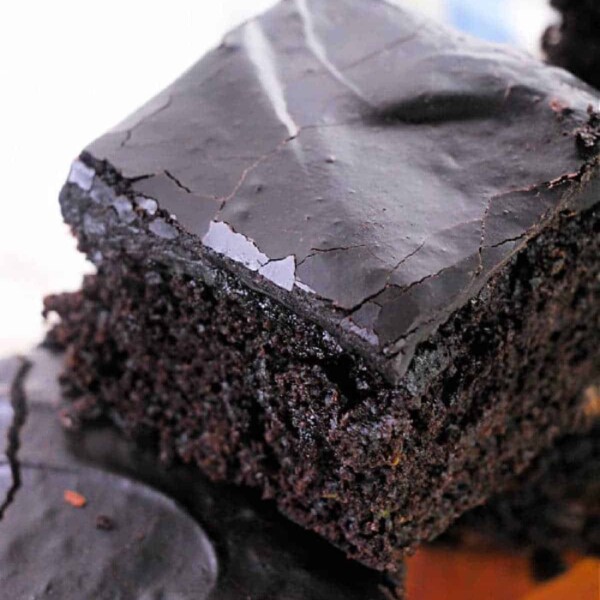 Close-up of a stack of chocolate brownies with a glossy, cracked top layer. Imagining these as part of a zucchini brownie recipe enhances their moist and dense texture, showcasing a rich, dark brown color.