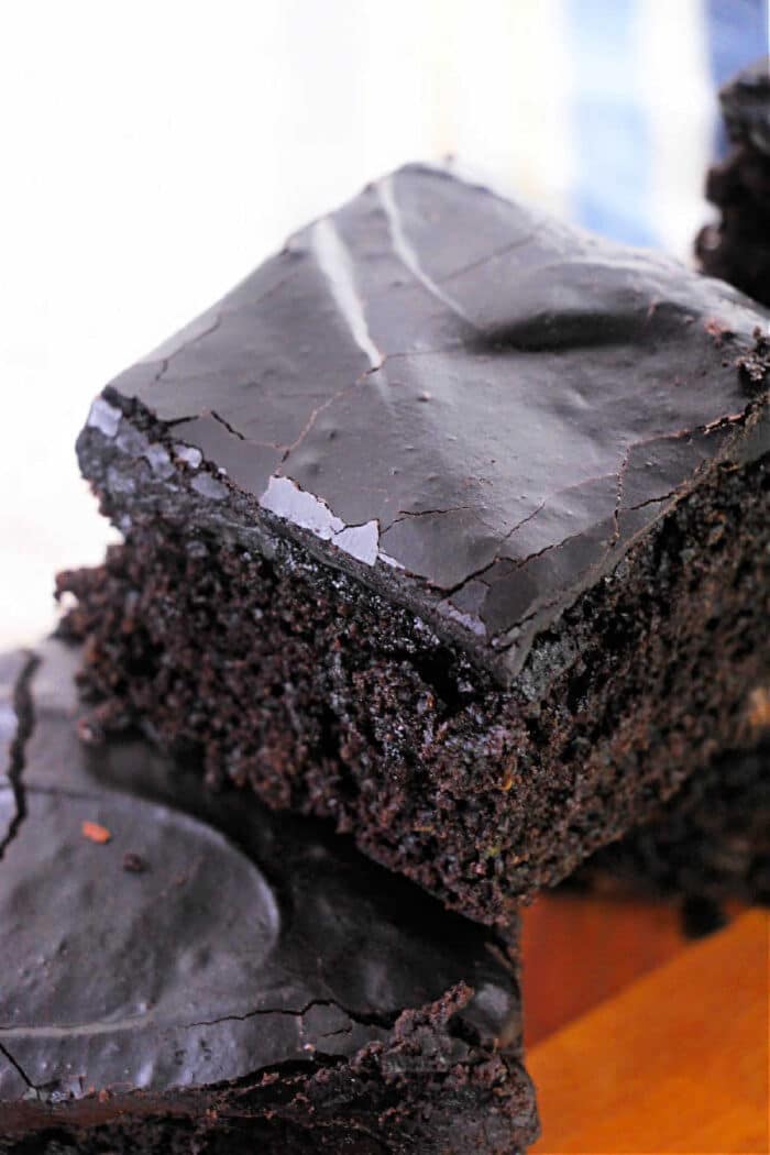 Close-up of a stack of chocolate brownies with a glossy, cracked top layer. Imagining these as part of a zucchini brownie recipe enhances their moist and dense texture, showcasing a rich, dark brown color.