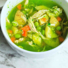 A comforting bowl of feel better soup, featuring peas, carrots, potatoes, and shredded chicken in a green broth, uses the convenience of an Instant Pot to bring warmth and nourishment to your table. Placed invitingly on a marble surface, it's perfect for those days when you need an extra hug.