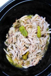 Pepperoncini chicken with shredded peppers simmers perfectly in a black slow cooker.