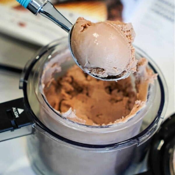 A hand holds an ice cream scoop filled with rich chocolate ice cream, poised above a container churned to perfection by the ninja creami machine.