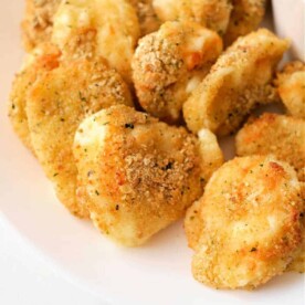 A plate of crispy, golden brown air fryer cheese curds, perfectly seasoned and mouth-wateringly delicious, with a small bowl of marinara sauce partially visible on the side.